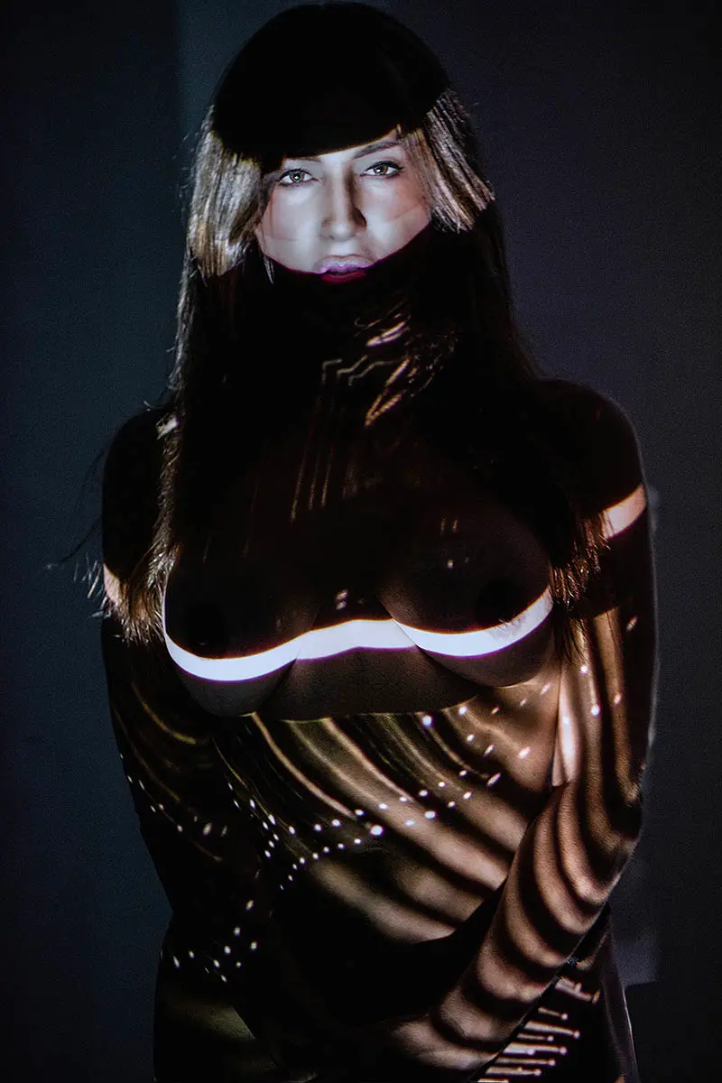 Female figure illuminated with intricate light projection patterns, art exhibition in Mykonos, Greece