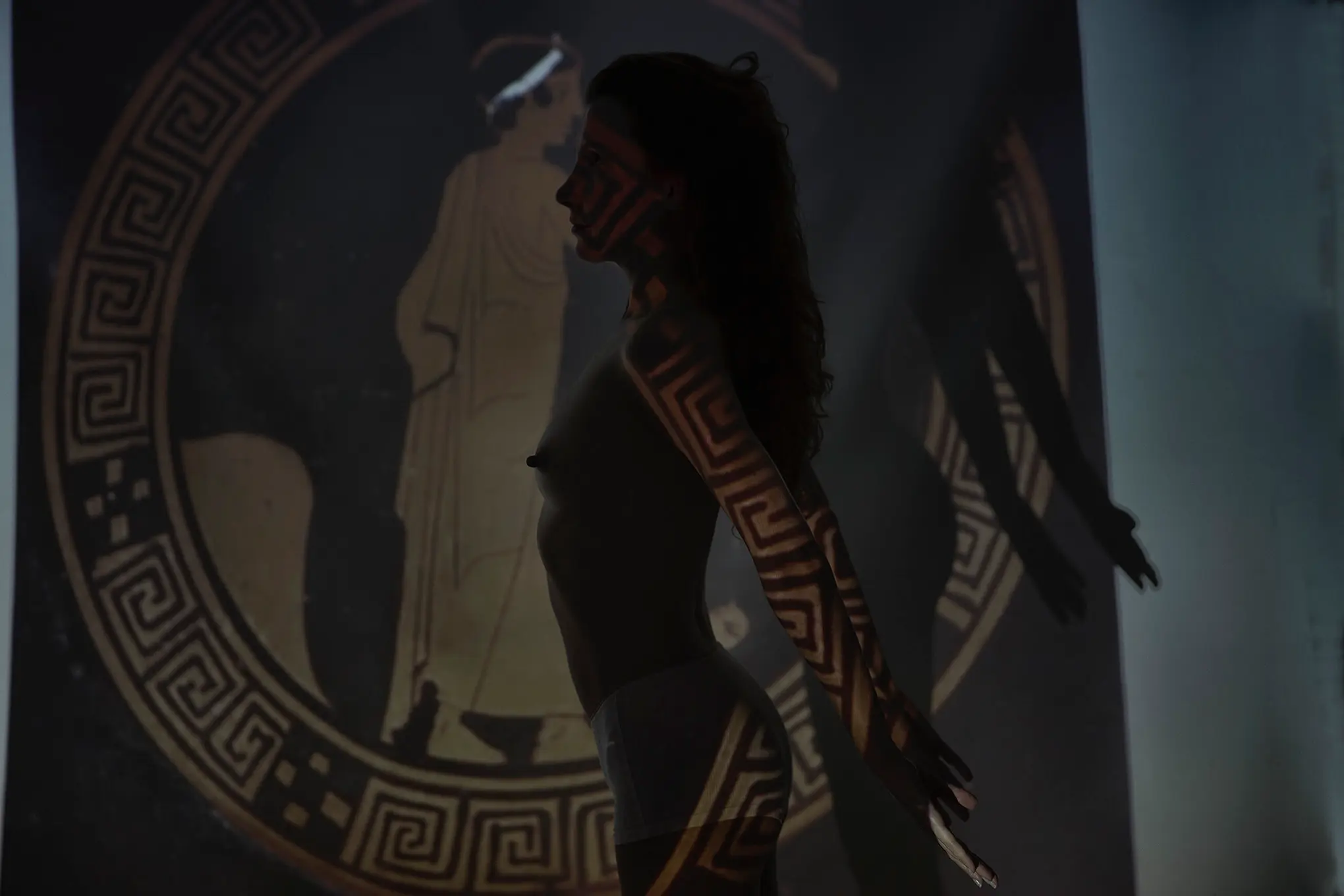 Silhouette of woman with Greek key pattern projection beside ancient vase, art exhibition in Mykonos, Greece