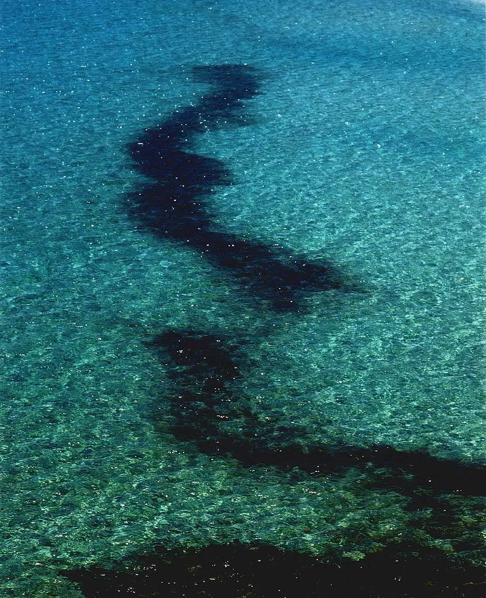 Aerial view of dark shadow drifting across clear turquoise sea, art exhibition in Mykonos, Greece