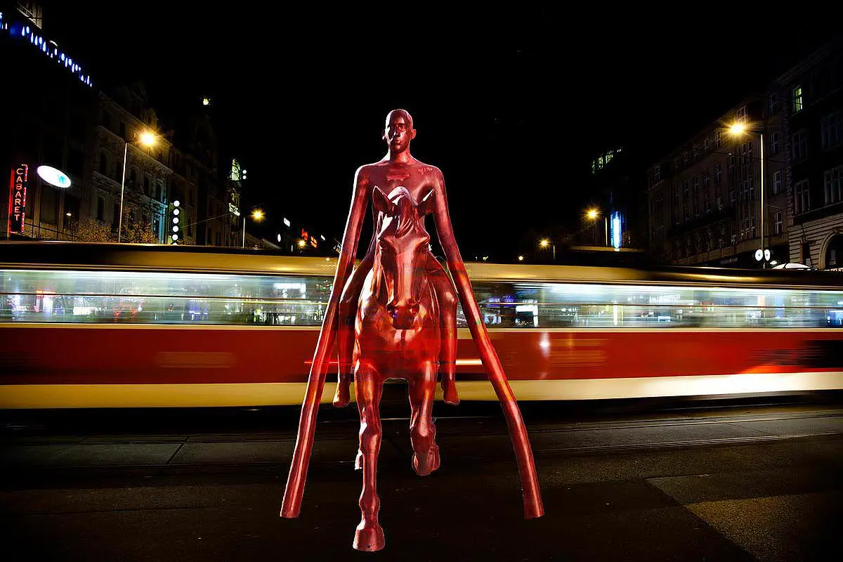 Red equestrian sculpture with tram light trails at night, urban art exhibition in Mykonos, Greece