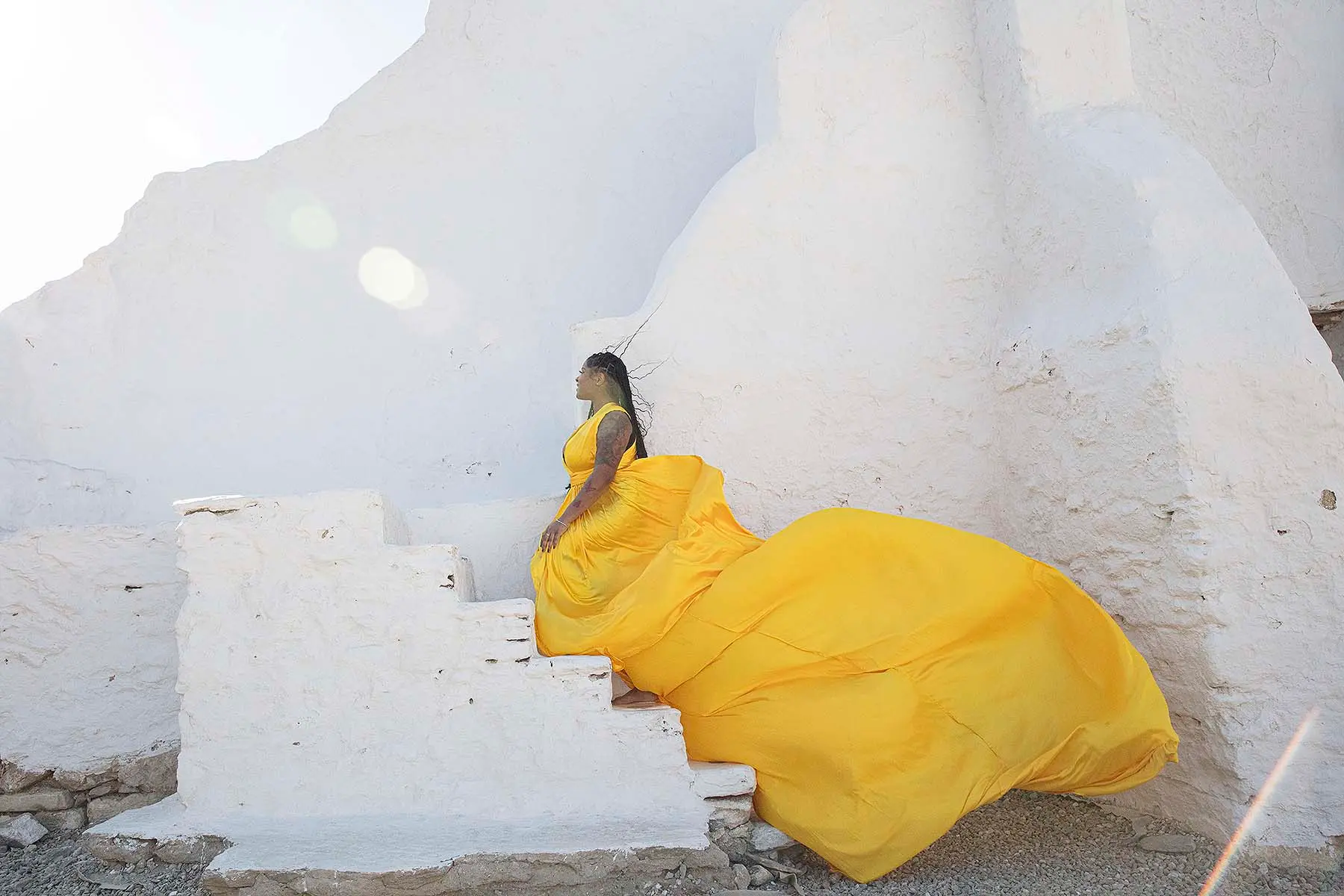 Sunlit amber flying dress in a Mykonos alley, photography in Mykonos, Greece