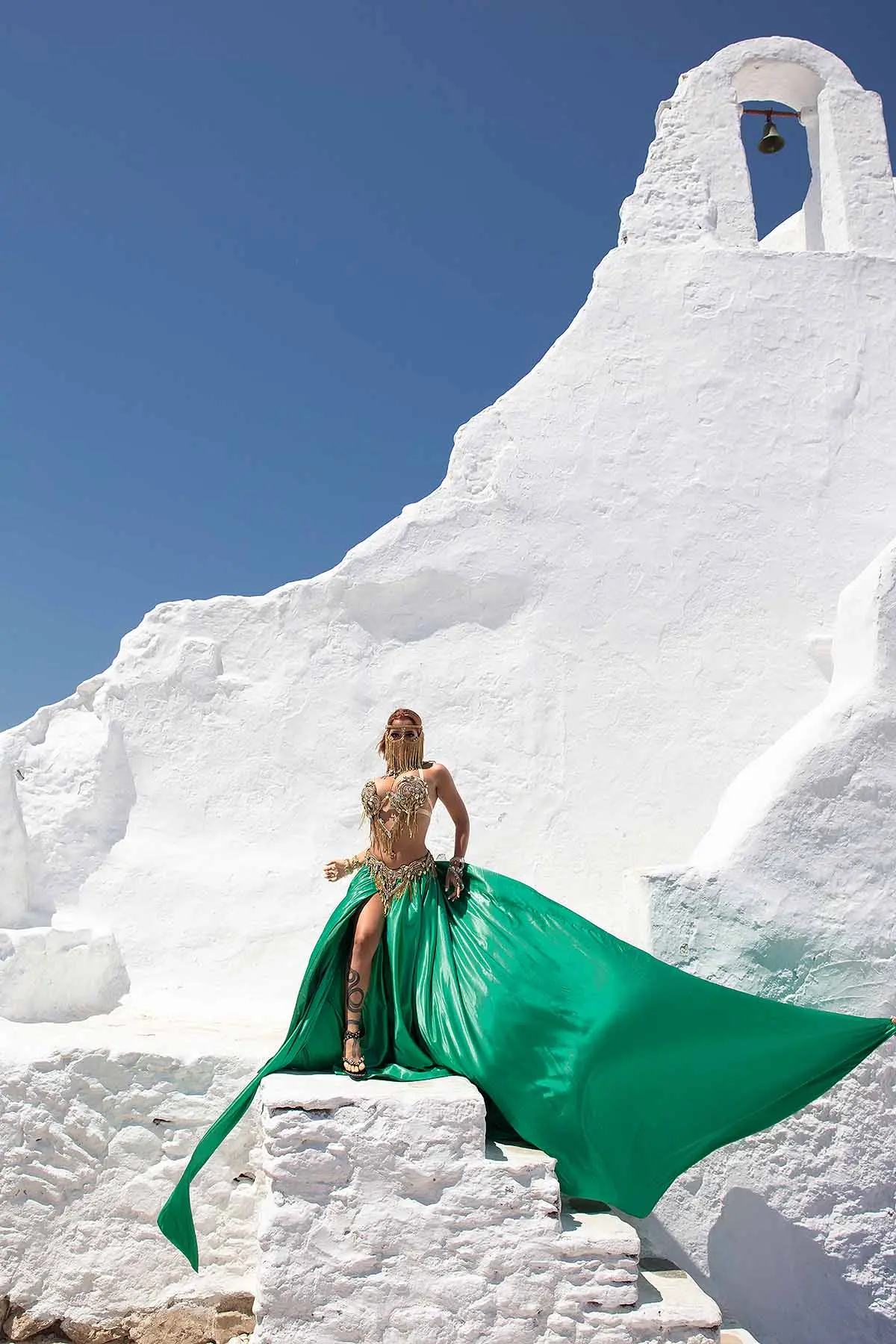 Sunlit coral flying dress at a Mykonos windmill, photography in Mykonos, Greece