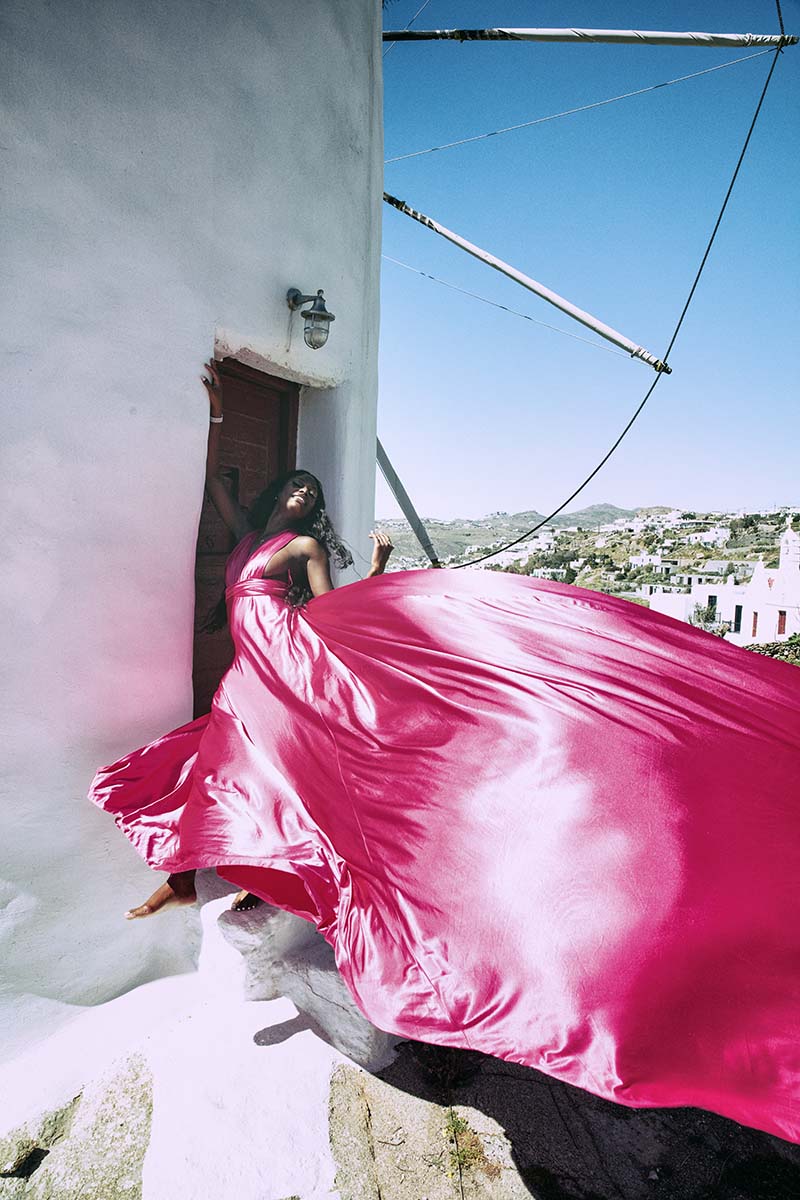 Sunlit dawn blush flying dress by Cycladic walls, photography in Mykonos, Greece