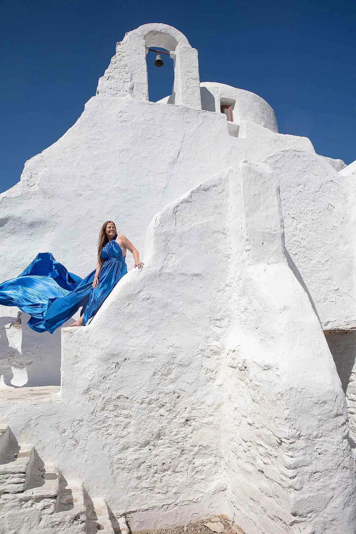 Sunlit emerald flying dress at a Mykonos windmill, photography in Mykonos, Greece