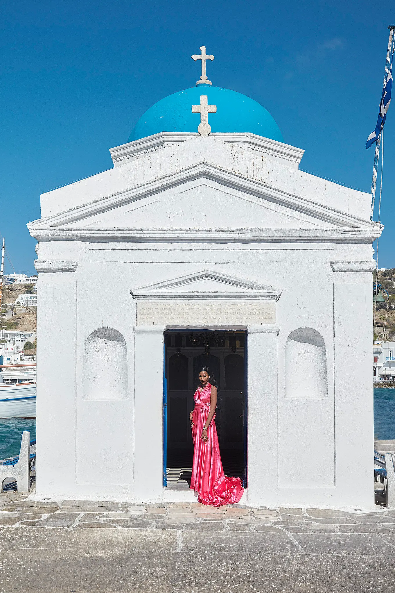 Sunlit fuchsia flying dress at Mykonos blue dome chapel in a Mykonos alley, photography in Mykonos, Greece