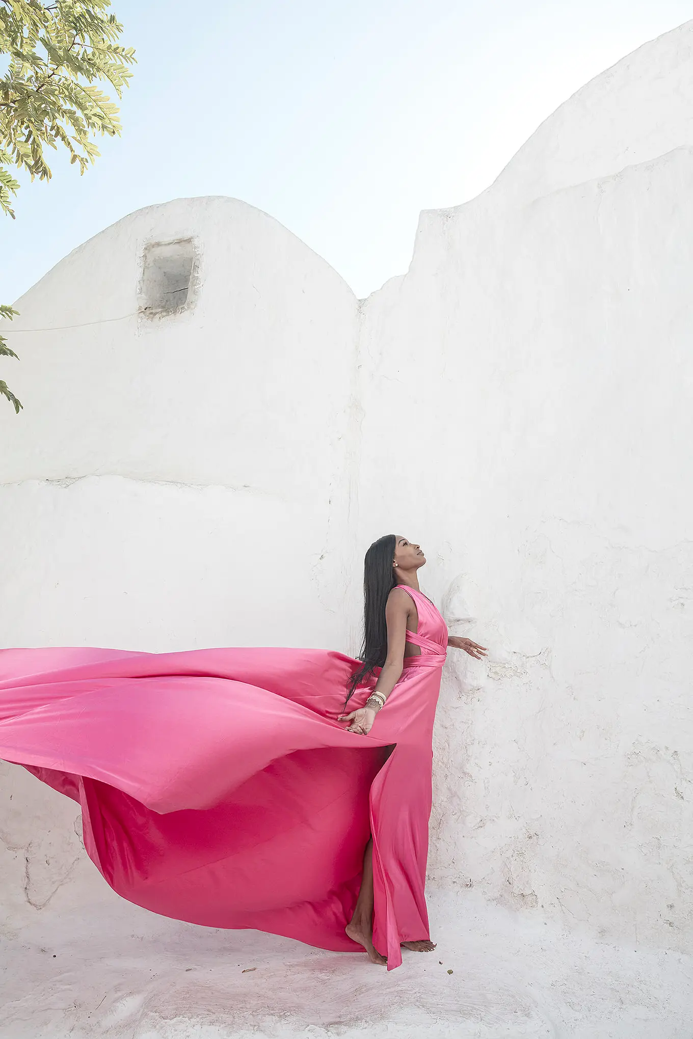 Sunlit fuchsia flying dress at Mykonos blue dome chapel by Cycladic walls, photography in Mykonos, Greece