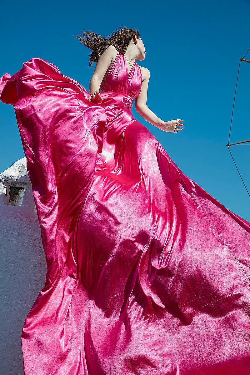 Sunlit fuchsia flying dress at Mykonos blue dome chapel near a whitewashed chapel, photography in Mykonos, Greece