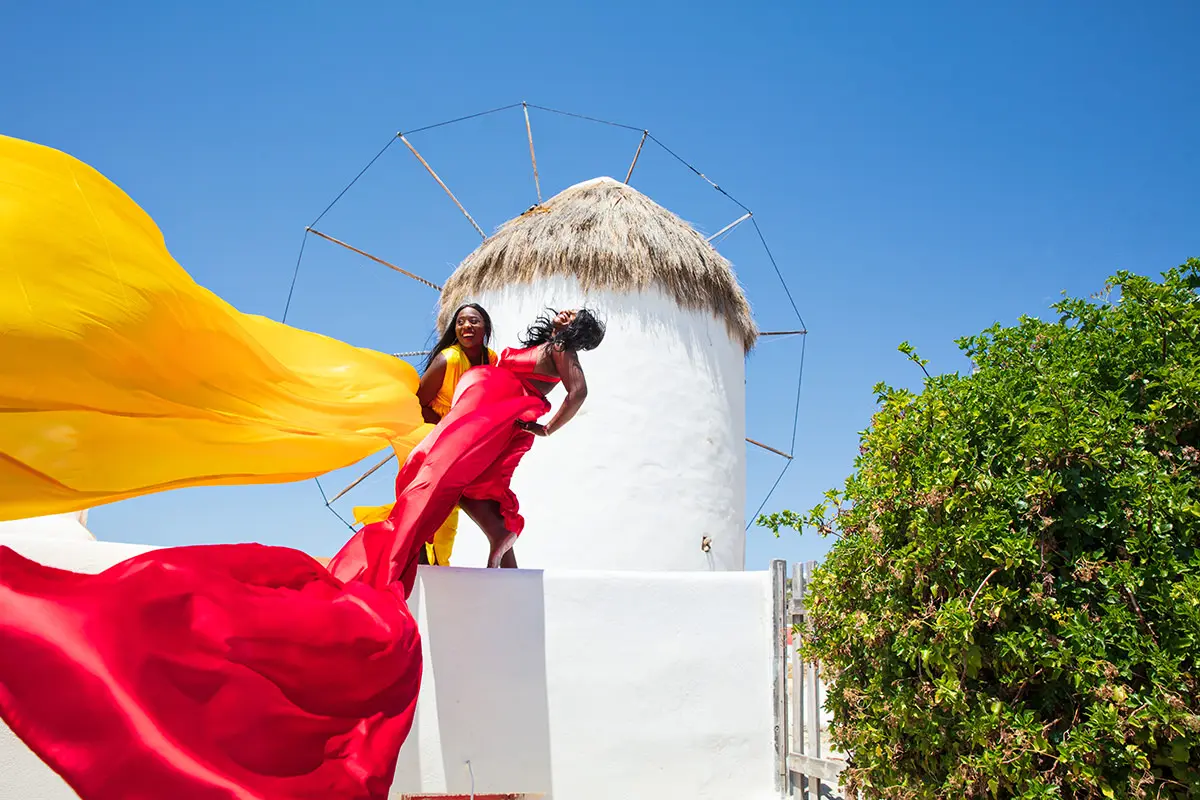 Sunlit gold flying dress near a whitewashed chapel, photography in Mykonos, Greece