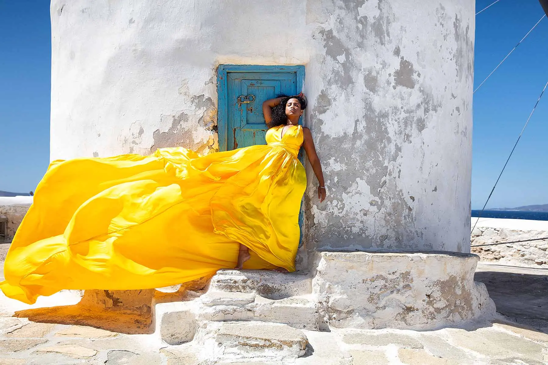 Sunlit violet flying dress at a Mykonos windmill, photography in Mykonos, Greece