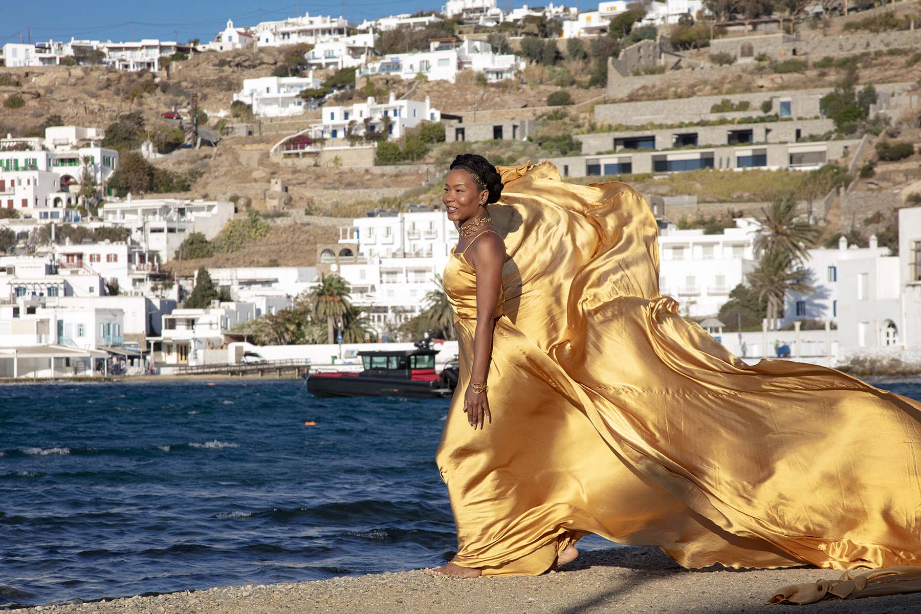 Sunlit red flying dress at white Mykonos chapel by Cycladic walls, photography in Mykonos, Greece