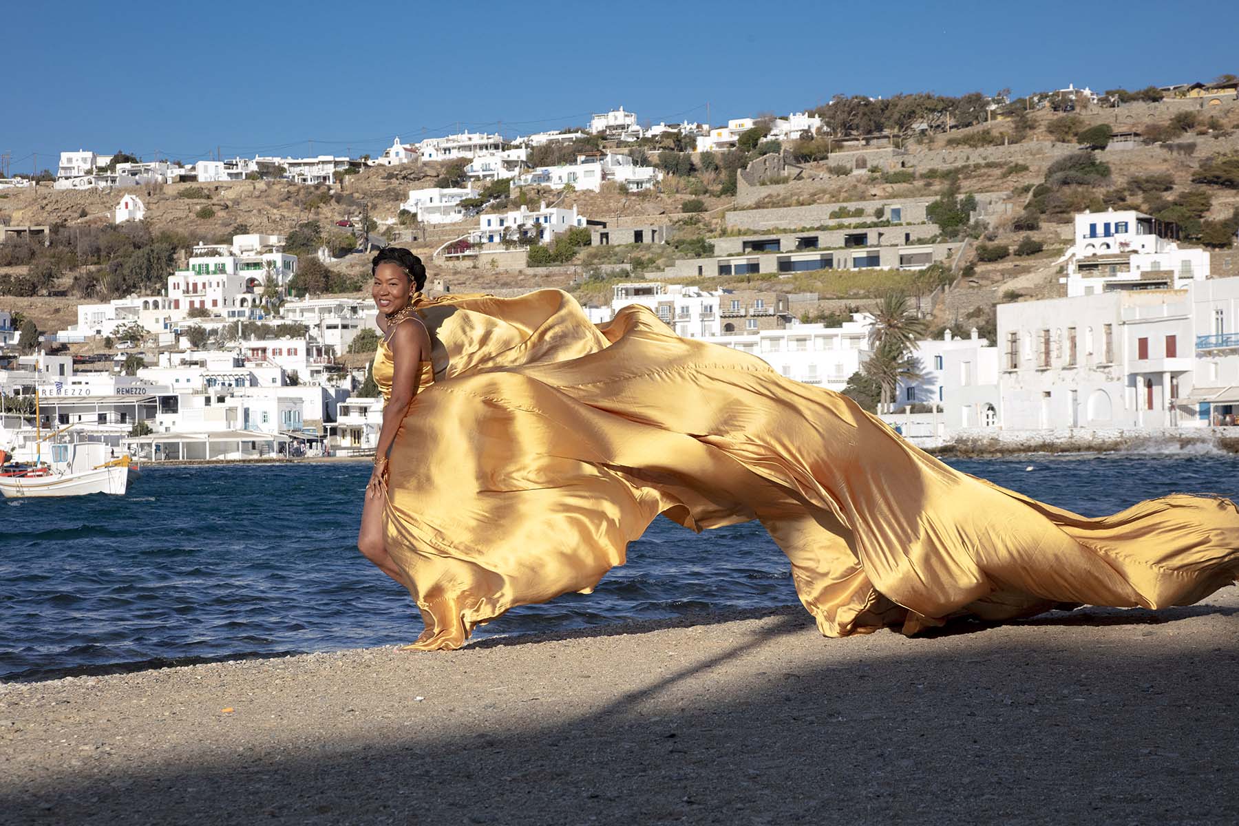 Sunlit red flying dress at white Mykonos chapel on a sunlit terrace, photography in Mykonos, Greece
